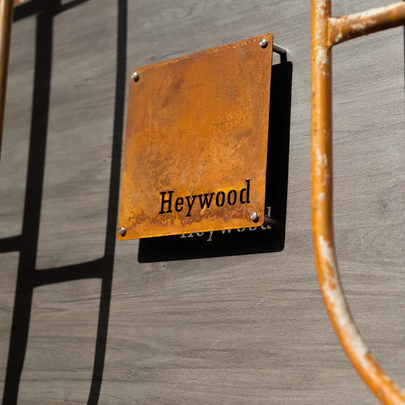 Rust-colored metal sign with 'Heywood' text on a wooden background