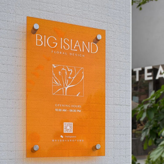 Orange signboard with 'BIG ISLAND FLORAL DESIGN' on a light gray wall.