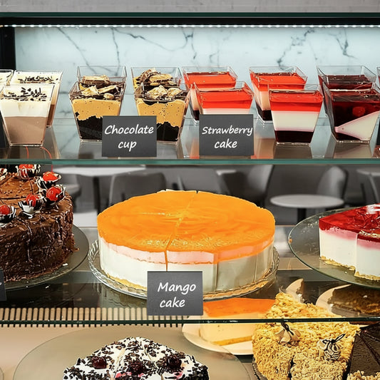 Display of various cakes including a mango cake, chocolate cup, and strawberry cake in a bakery.