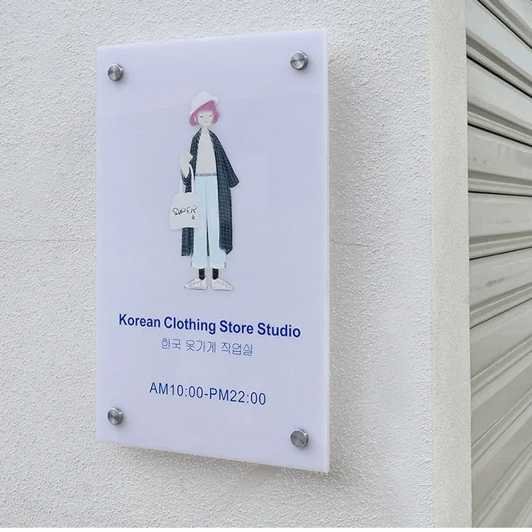 Plaque for Korean Clothing Store Studio with store hours on a textured wall.